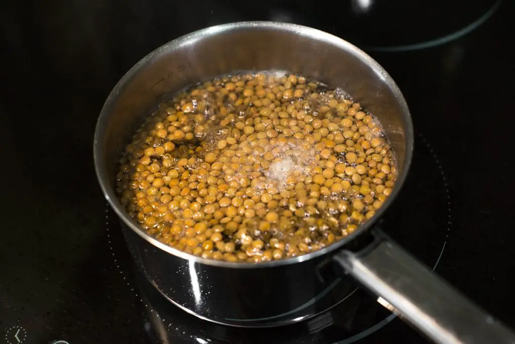 Green lentils cooking in a pan of boiling water.